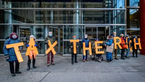 Getty Images Protesters hold signs saying tax the rich