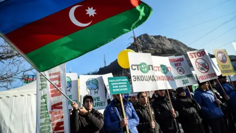 TOFIK BABAYEV/AFP An Azerbaijani environmental activist waves a national flag during a protest against what they claim the illegal mining at the Lachin corridor, the Armenian-populated breakaway Nagorno-Karabakh region's only land link with Armenia, on December 27, 2022