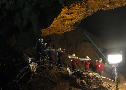 Pongmanat Tasiri/EPA Thai officials carry oxygen tanks through a cave complex during a rescue operation for a missing football team at the Tham Luang cave in Tham Luang Khun Nam Nang Noon Forest Park in Chiang Rai province, Thailand, 30 June 2018