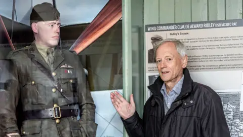 Dave Davies/SMGWA Nick Kitto is standing next to a wax work model of his grandfather Claude Ridley. Nick's hand is gesturing toward him. The waxwork model is wearing full military uniform, while Nick is wearing a dark coloured jacket and a shirt underneath.
