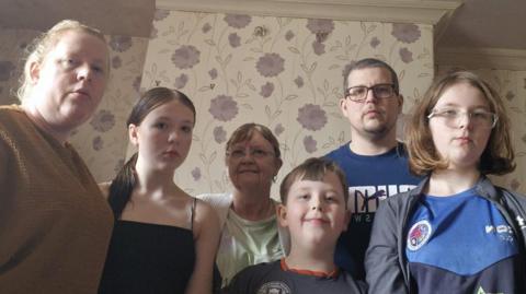 Family standing in their home, after builder left it without finishing work.