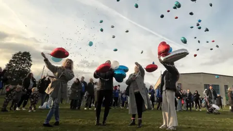 Jules Hyam/BBC Four women stand on an area of parkland in Bristol releasing balloons. Behind them are many more people also releasing balloons of different colours