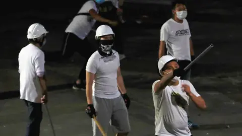 Getty Images Masked men in white T-shirts, armed with sticks, after they attacked anti-extradition bill protestors after a demonstration. Yuen Long, Hong Kong