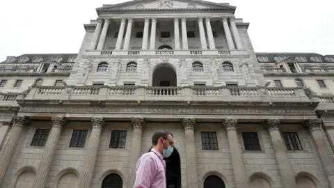 Reuters Man wearing a mask walks passed the Bank of England in the City of London