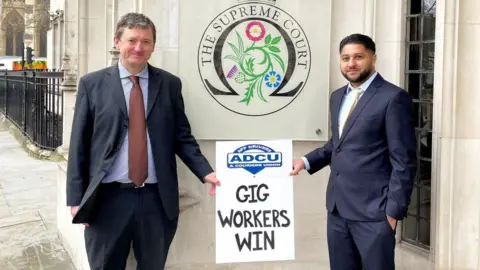 ADCU Union Former Uber drivers James Farrar and Yaseen Aslam pose in front of the Supreme Court on Friday