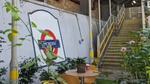 TfL Leaves and foliage provide camouflage for metal poles and a staircase at Morden station.