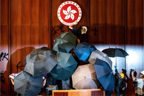 Getty Images A protester defaces the Hong Kong emblem after protesters broke into the government headquarters in Hong Kong on 1 July 2019, on the 22nd anniversary of the city's handover from Britain to China