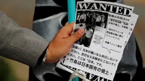 Reuters A man holds leaflets denouncing South Korean boy band BTS outside Tokyo Dome