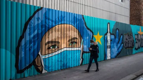 EPA A pedestrian walks past a street-art mural by French artist JBC, in tribute to health workers representing a nurse wearing a protective face mask in front of a hospital in Paris, France, 20 March 2021