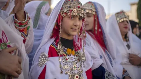 EPA Amazigh women and girls wear traditional clothes to present food during celebrations on the eve of the 2973th Amazigh New Year, near the parliament in Rabat, Morocco, 13 January 2023. After more than eleven years of devoting Berbers as an official language alongside Arabic, voices in Morocco are increasingly calling for a public holiday to celebrate the Berber New Year.The term 'Yennayer' is also the name given to the first month of the Amazigh calendar.