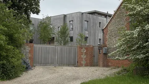 Arcady house, showing wooden structured house behind closed wooden gate and gravel driveway