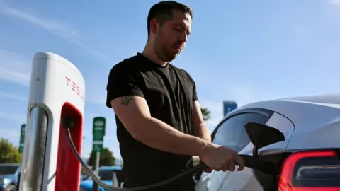 Getty Images Robert Chavez plugs in his Tesla electric cars to recharge at a Tesla Supercharger station on January 16, 2024 in Burbank, California.