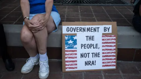 Getty Images A woman sits by a sign that says "Government for the people not the NRA"