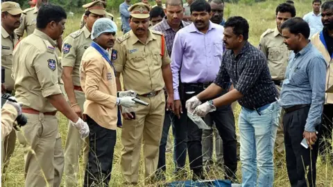Getty Images forensic official ((3L) holds a gun as police officers gather around the body of man at the site where Police officers shot dead four detained gang-rape and murder suspects in Shadnagar, some 55 kilometres (34 miles) from Hyderabad, on December 6, 2019.
