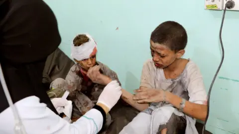 Reuters A doctor treats children injured by an air strike in Saada, Yemen (9 August 2018)