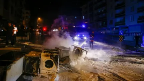 Reuters A firefighter extinguishes goods of a shop burnt during riots against refugees in Ankara, Turkey