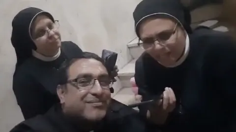 Vatican News Sister Nabila Saleh (R) and Father Yusuf Asad (C) talk to the Pope by telephone from Gaza City's Holy Family Church