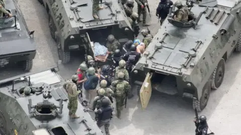 Reuters Two handcuffed men with shirts over their heads are moved into tanks by Ecuador police