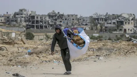 A displaced Palestinian man carries his belongings while walking along a street in Khan Younis, in the southern Gaza Strip (24 March 2024)