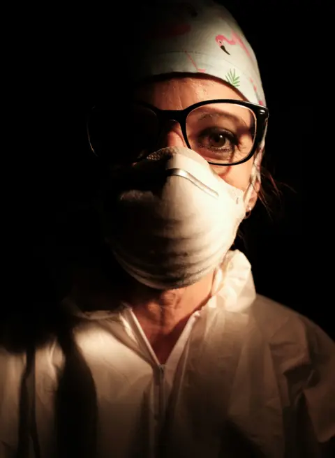 Paolo Miranda A female nurse wearing a face mask with a dark background behind her