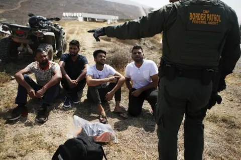 Getty Images A U.S. Border Patrol agent monitors a group of apprehended males from India who illegally crossed the U.S.-Mexico border on July 16, 2018 in San Diego, California. The entire Southwest border saw 34,114 U.S. Border Patrol apprehensions in the month of June compared with 40,338 in May.