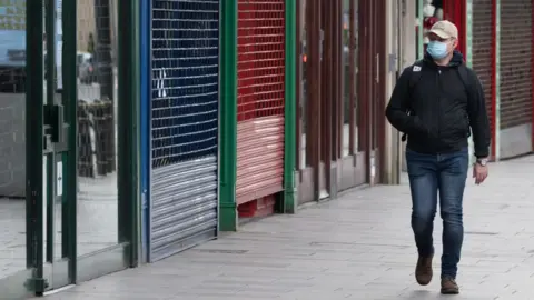 Matthew Horwood Man in mask walks past empty shops