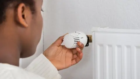 Getty Images Woman adjusting temperature of radiator using thermostat