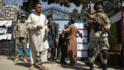 Getty Images Security forces search voters as they enter a polling station in Kabul