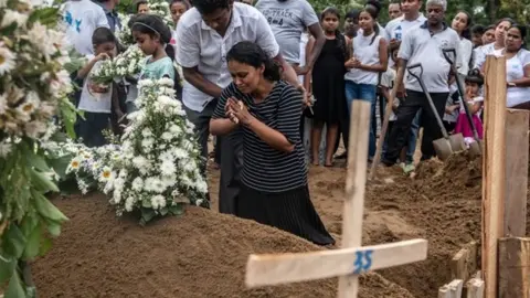 Getty Images A woman grieves at the grave after a funeral for a person killed in the Easter Sunday attack on St Sebastian"s Church, on April 25, 2019