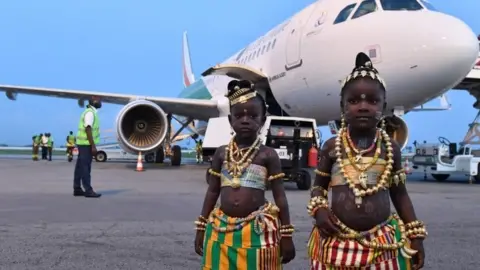 AFP Two young girls in traditional dress pose in front of the tenth airplane of Ivory Coast's national carrier Air Cote d"Ivoire, a new generation Airbus A320, during a ceremony at Felix Houphouet-Boigny airport in Abidjan on July 18, 2017.