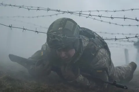 VIACHESLAV RATYNSKYI / REUTERS A new recruit to Ukraine's army crawls under wire