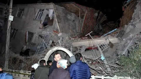 Reuters People stand outside collapsed building - 24 January