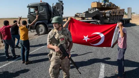 Getty Images People hold a Turkish flag as they give their support to the Turkish military during the deployment of tanks to Syria