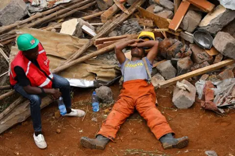 EPA An emergency responder takes a nap on top of rubbles as the search and rescue for survivors through the rubbles of a collapsed six-storey building continues in Kirigiti town, in Kiambu, Kenya, 26 September 2022. Local media reported that three people died and several people are feared trapped as the rescue operation continues.