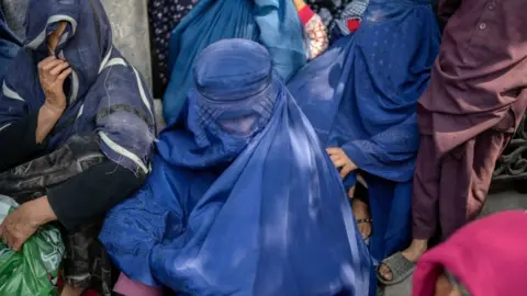 BULENT KILIC/AFP Women wait in front of a bank to withdraw money in Kabul.