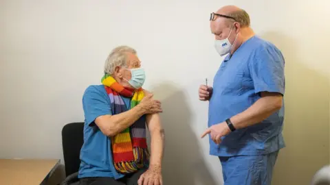 PA Wire Sir Ian McKellen talking to a GP about the vaccine