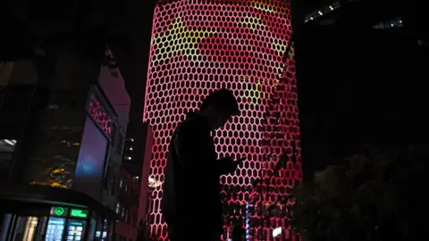 Getty Images A man looks at his phone near a giant image of the Chinese national flag on the side of a building in Beijing in 2017