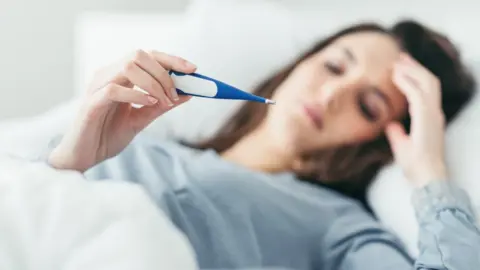 Getty Images Woman in bed with thermometer (Posed by model)