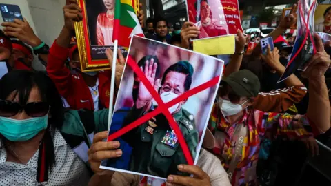 Reuters Protesters hold up a picture of Myanmar's army chief Min Aung Hlaing with his face crossed out and pictures of Aung San Suu Kyi, during a demonstration to mark the second anniversary of Myanmar's 2021 military coup, outside the Embassy of Myanmar in Bangkok, Thailand