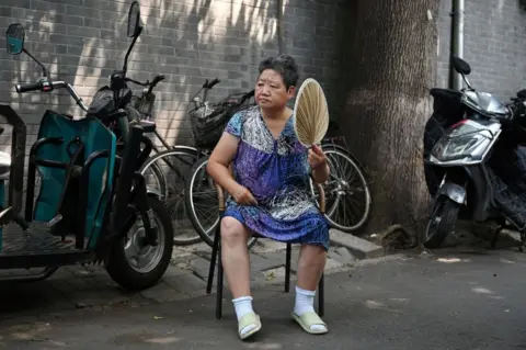 Greg Baker / AFP A woman fans herself while resting in the shade in an alley during a heatwave in Beijing