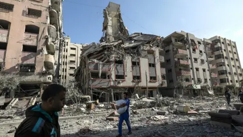 EPA Palestinians walk past damaged buildings in Gaza City's Tal al-Hawa district (30 October 2023)