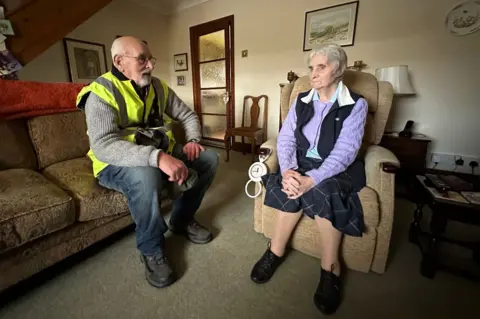 A man on a sofa talks to a woman in an arm chair