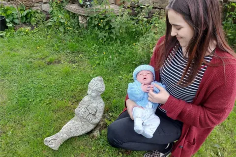 Maggy Young Daisy holds Elijah next to gnome