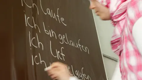 Girl in a headscarf writing in German on a blackboard