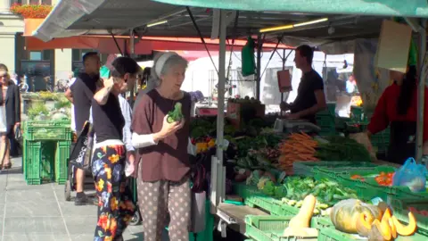 BBC A number of people examine fresh produce at a farmer's market