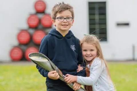 Getty Images Seven-year-old Harrison Shaw and his four-year-old sister Harper with the baton at the Lochranza Distillery