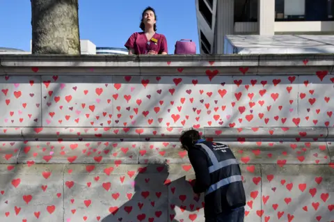 Toby Melville / Reuters A health worker stands behind a wall painted in hearts, on 29 March 2021