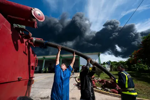 Yamil Lage / AFP Firefighters work near a massive fire at a fuel depot sparked by a lightning strike in Matanzas, Cuba, on 8 August 2022