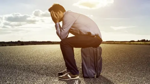 Getty Images Man sits on suitcase