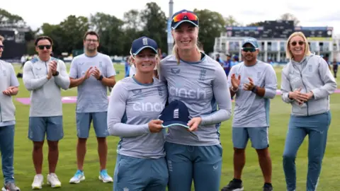 ECB/Getty Images England's Freya Kemp (R) is presented with her debut cap by team mate Danni Wyatt (L)